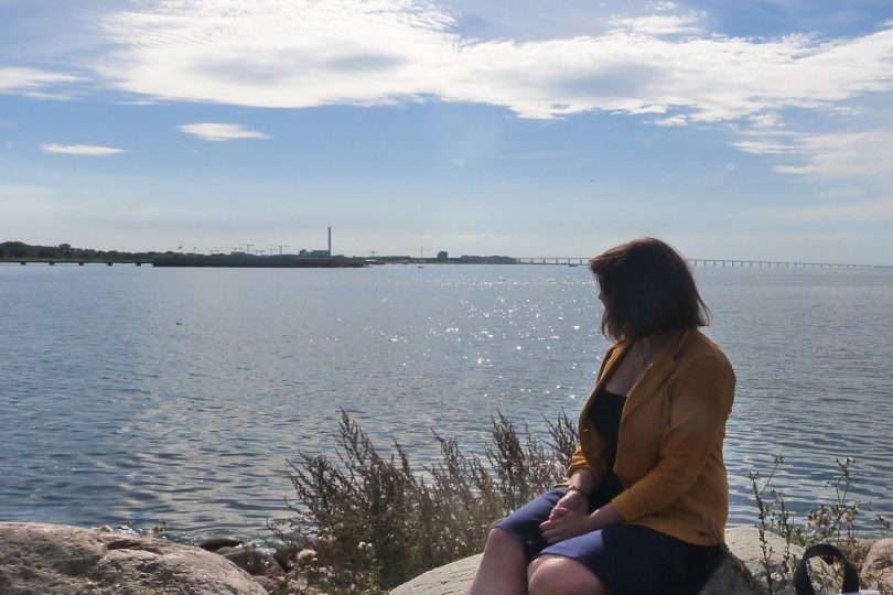 Die Studentin Elisaveta Lebedeva sitzt auf einem Felsen und blickt auf die Öresundbrücke.