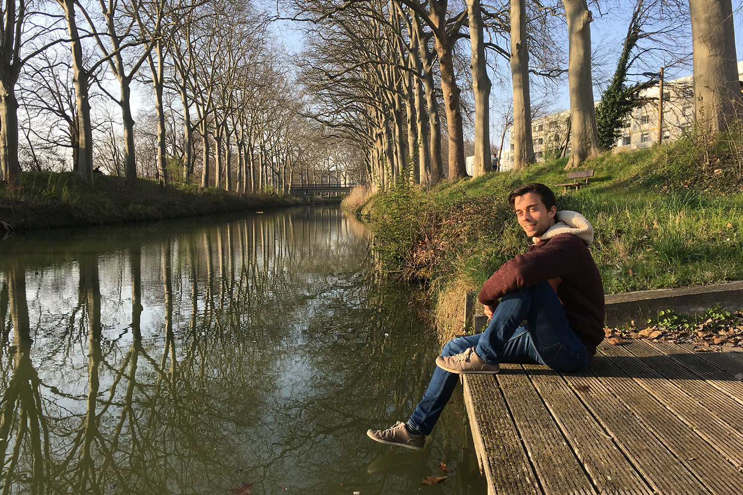 Der Student sitzt auf einem Holzsteg an einem Fluss.