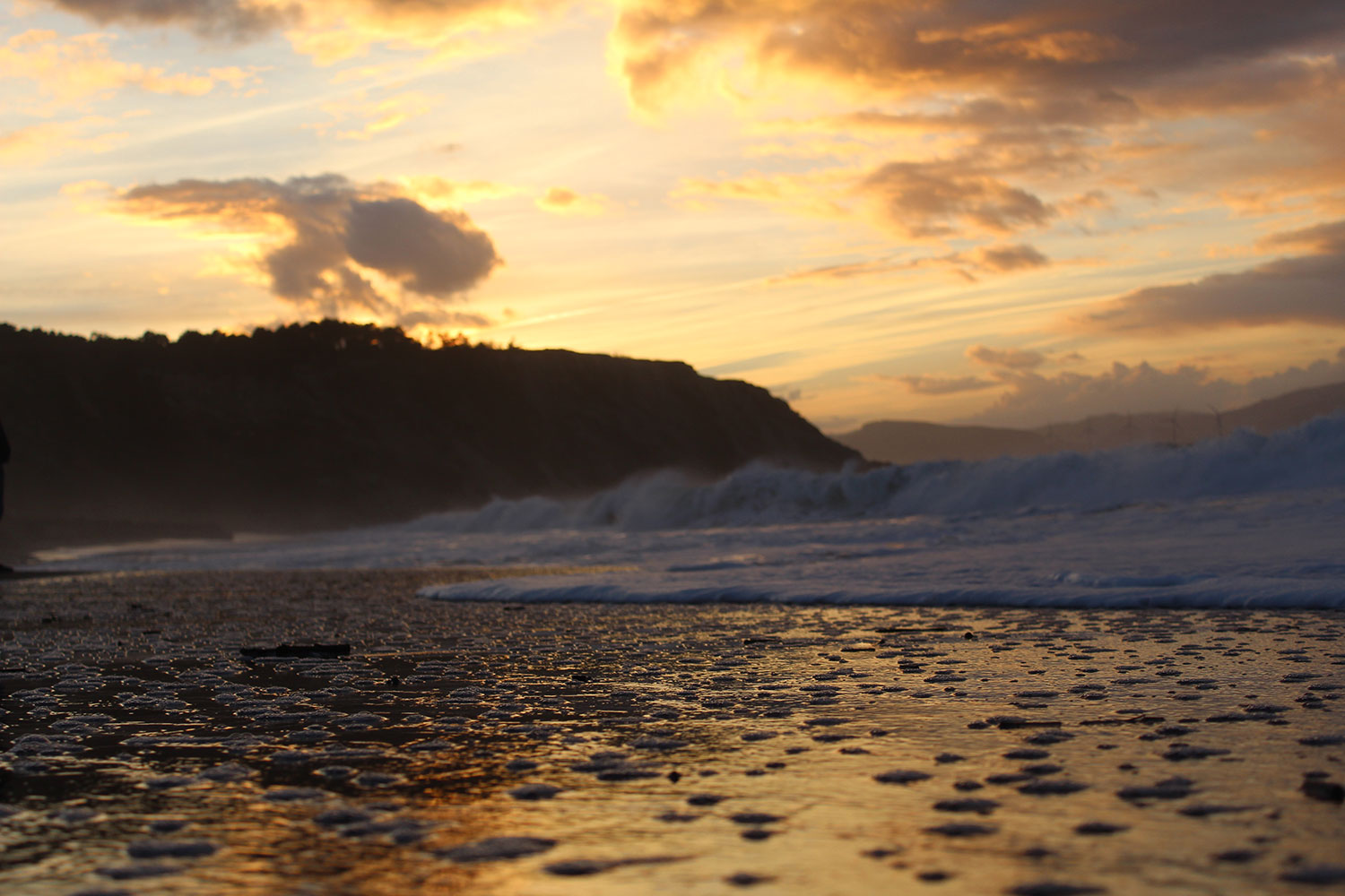 Zu sehen ist ein Strand in der nähe von Bilbao bei Sonnenuntergang. Die Brandung ist in Nahaufnahme zu sehen.