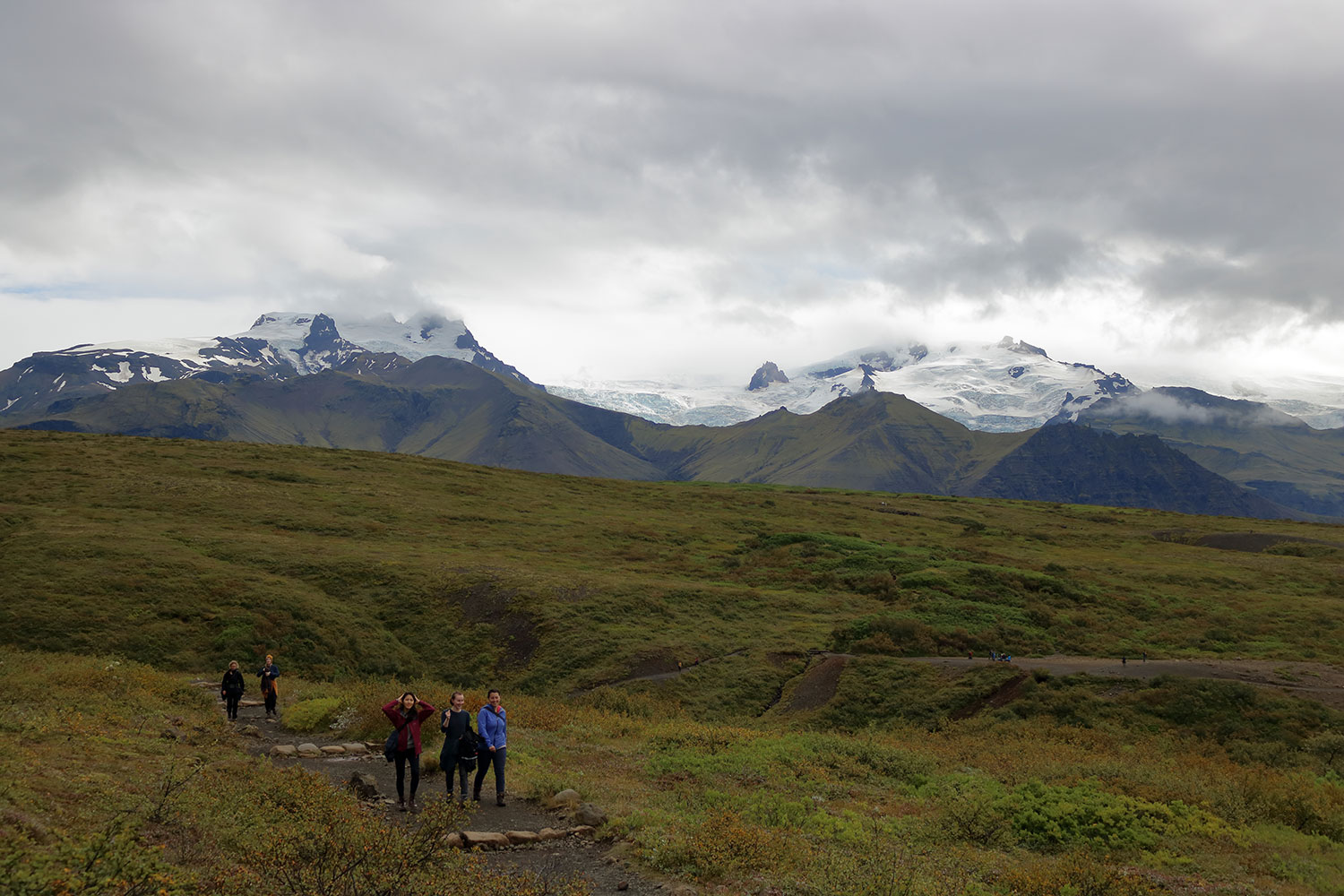 Mehrere Personen wandern duch eine isländische Hügellandschaft.