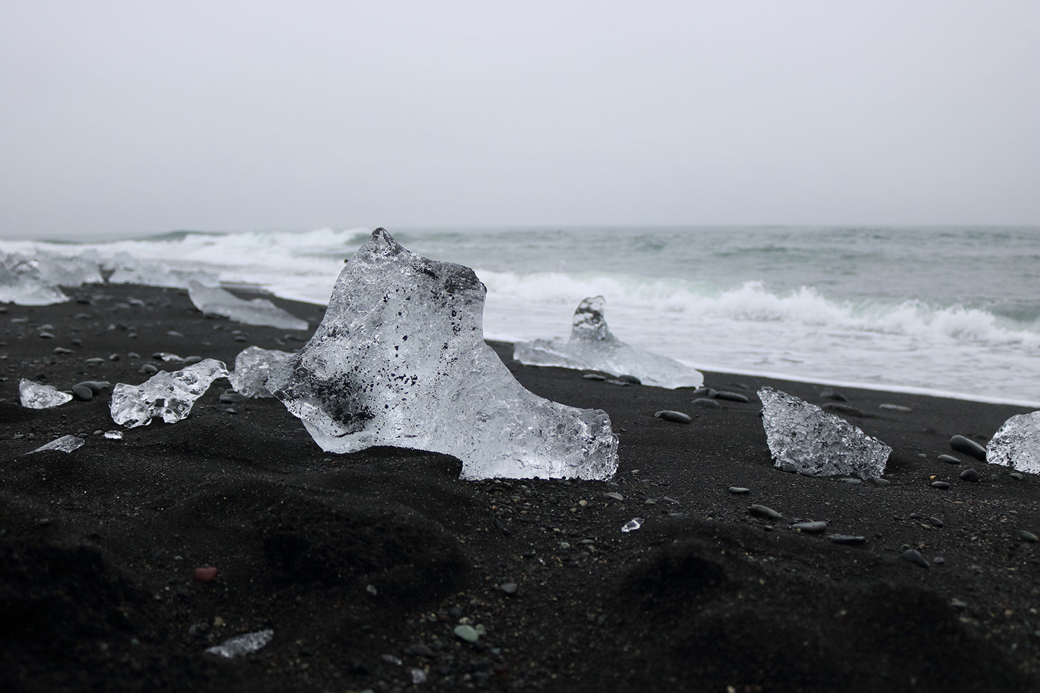 Zu sehen ist ein schwarzer Sandstrand und Wellen im Hintergrund.