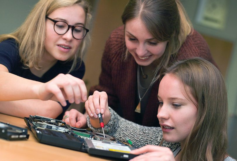 Zu sehen sind drei junge Frauen, die gerade an einem technischen Gerät arbeiten.