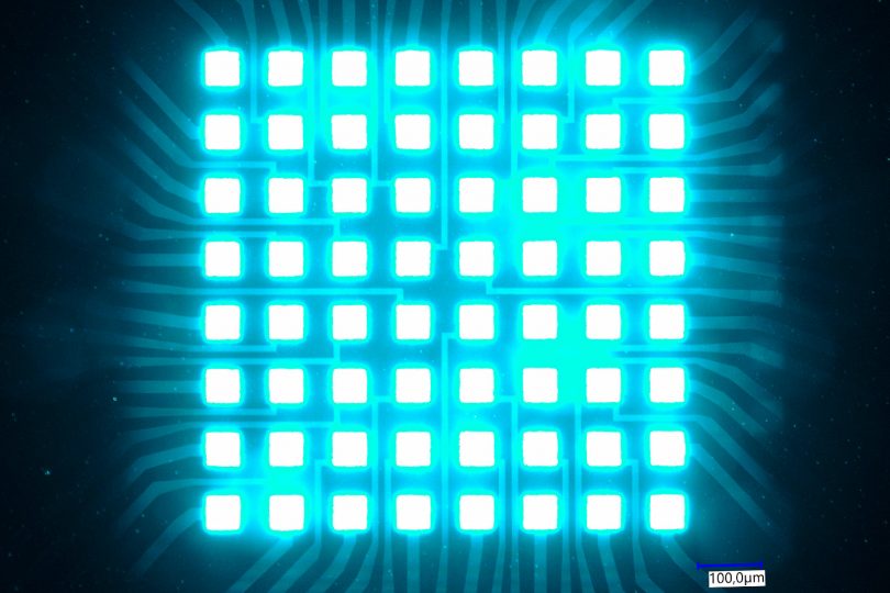 Acht mal acht mikroskopische LEDs leuchten hell in cyan. Bei dem Chip für Quantencomputer wären lediglich feine Lichtstrahlen erkennbar.