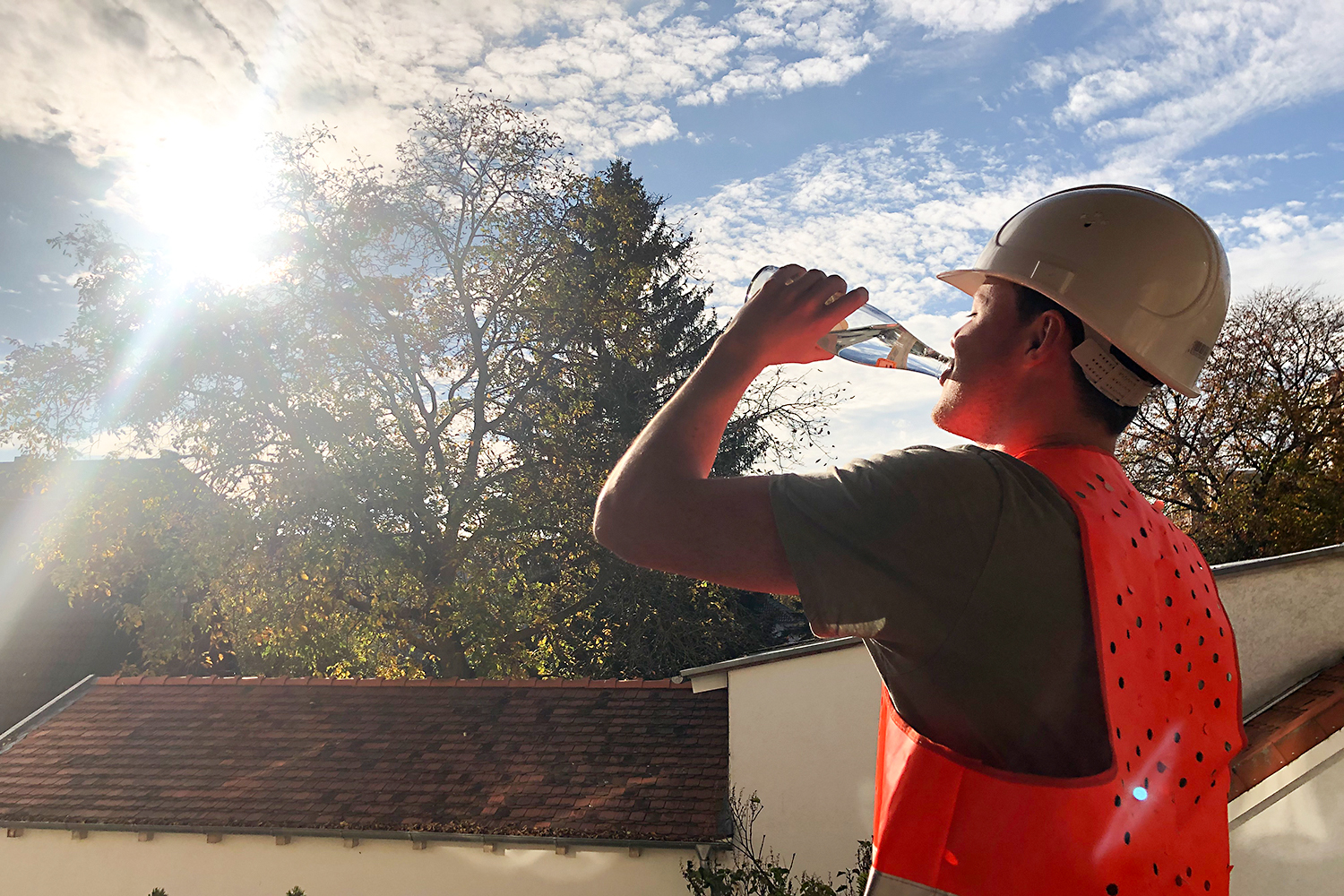 Ein Bauarbeiter mit Helm und Warnweste trinkt aus einer Wasserflasche.