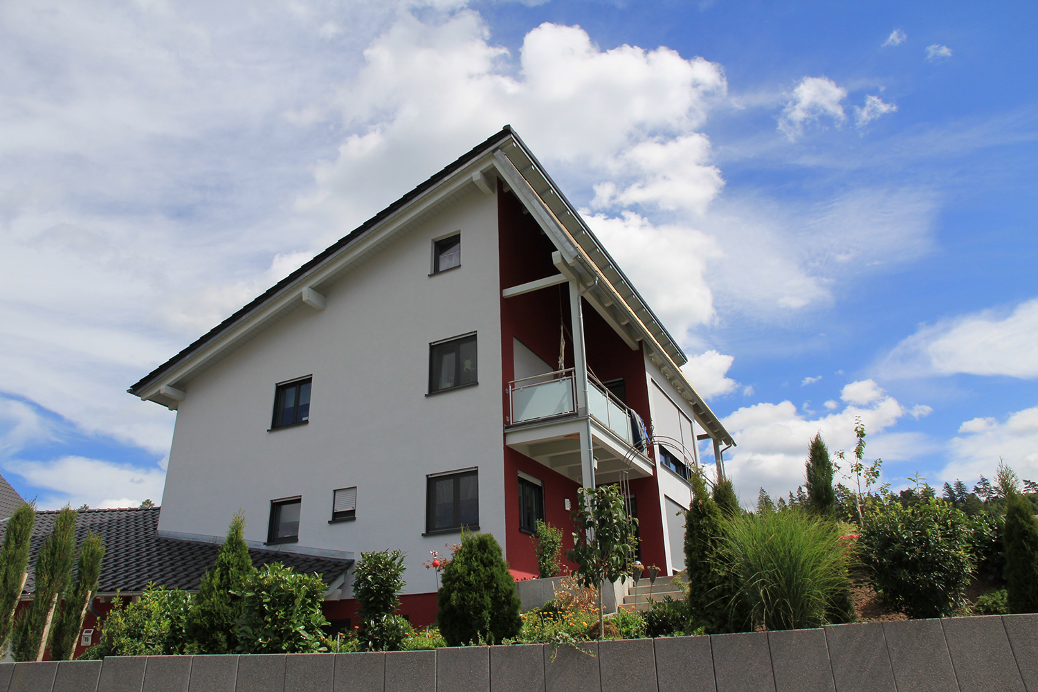 Zu sehen ist ein Haus mit Garten. Die Fassade ist verputzt und zweifarbig gestrichen. 