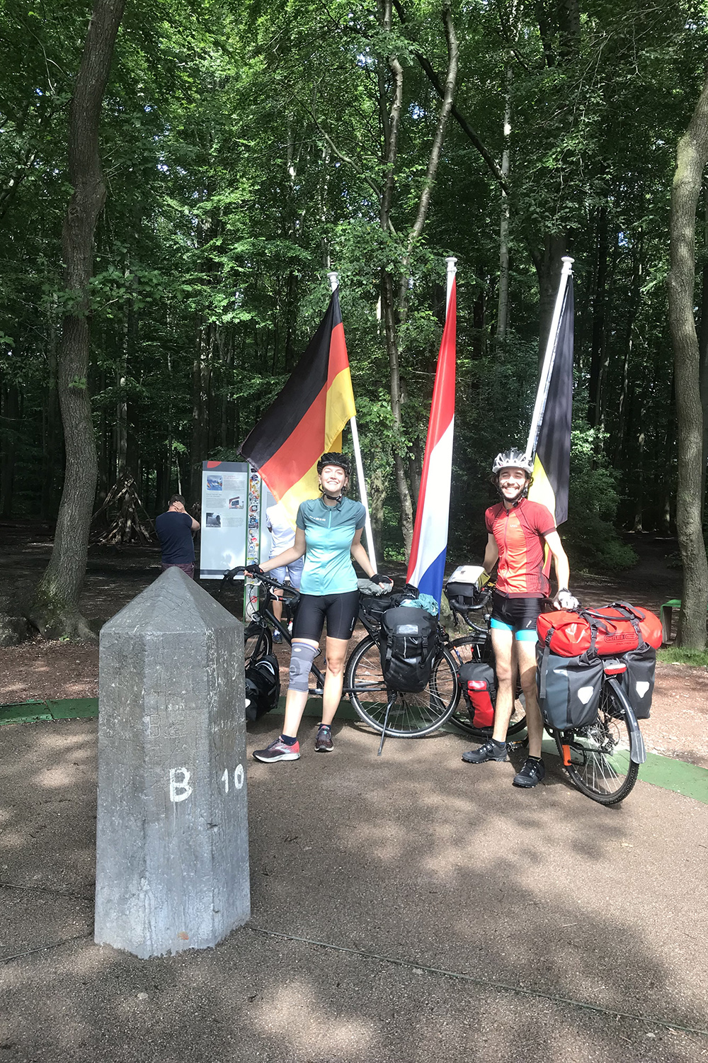 Moses Köhler and his girlfriend stand with their bikes in front of the German, Belgian and Dutch flags.