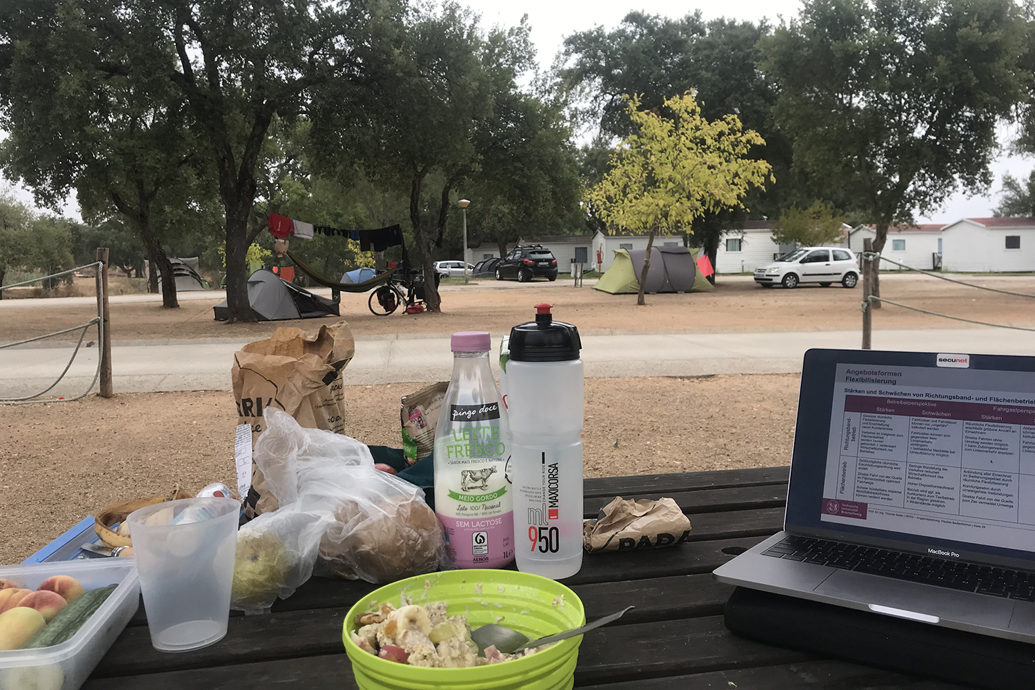 Auf einem Campingtisch stehen ein Laptop und Snacks.