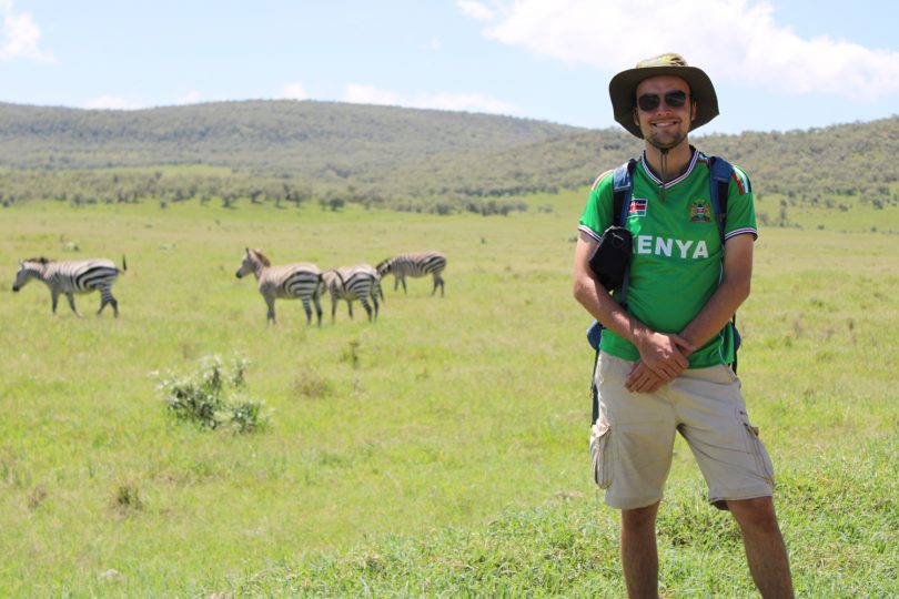 Der Student Nils Michalke steht in der afrikanischen Steppe. Im Hintergrund sind Zebras zu sehen.